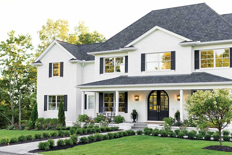 Exterior of a white traditional home with black shutters in New England, featuring Marvin Essential windows and doors.