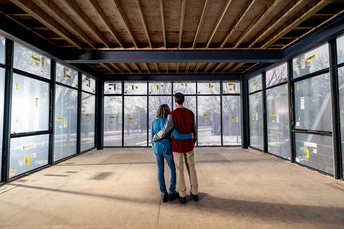 Two people standing in their modern home build looking through three walls of floor to ceiling Marvin Modern windows.