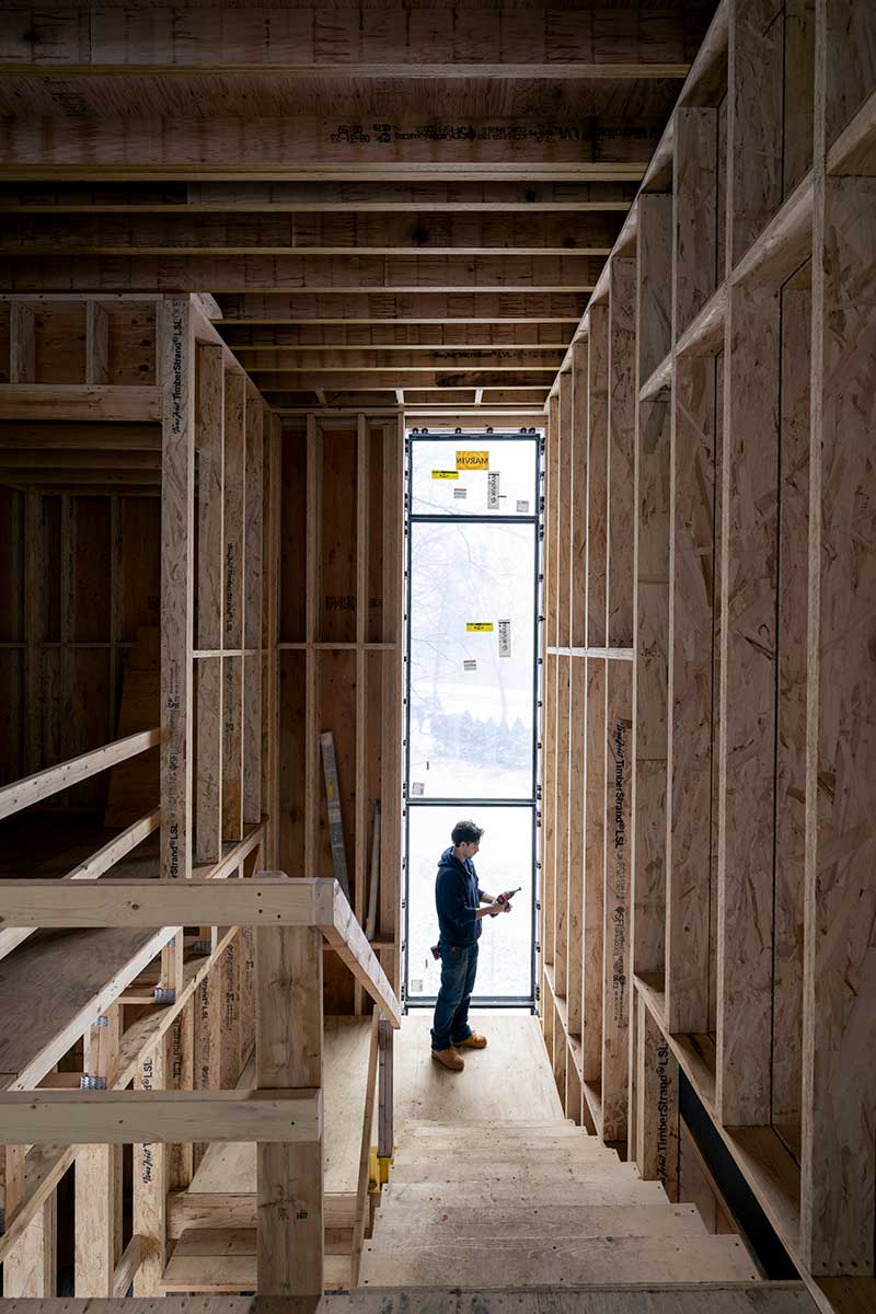 A contractor standing at the bottom of a staircase inside a work-in-progress custom home build.