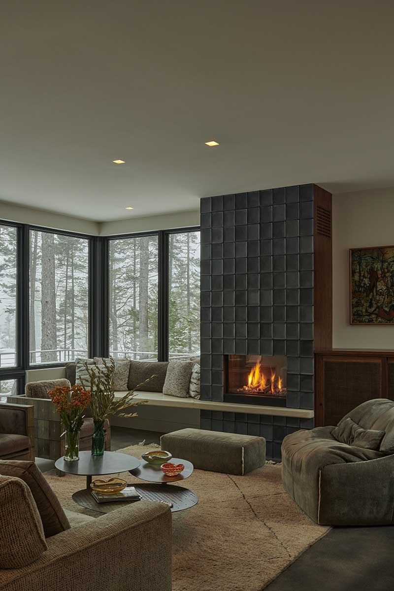 A modern living room with concrete fireplace, featuring Marvin Ultimate windows looking out on a snowy forest landscape.