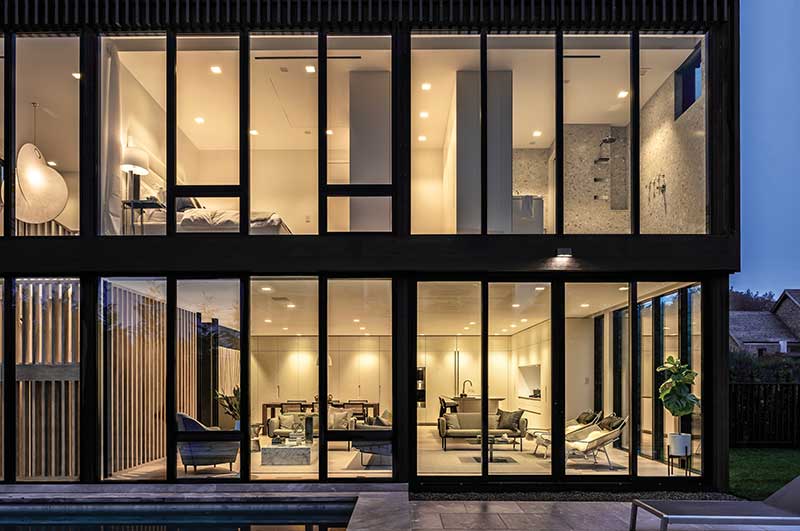 A modern home in Sag Harbor, New York, featuring Marvin Modern windows and doors on two floors looking into a living room and kitchen on the first floor and bedroom on the second.