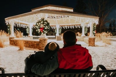 A couple sitting on a bench looking at a gazebo in the snow