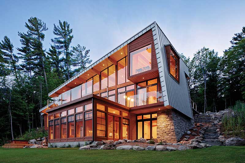An exterior photo of a contemporary home with a wall of windows, brightly lit from within.