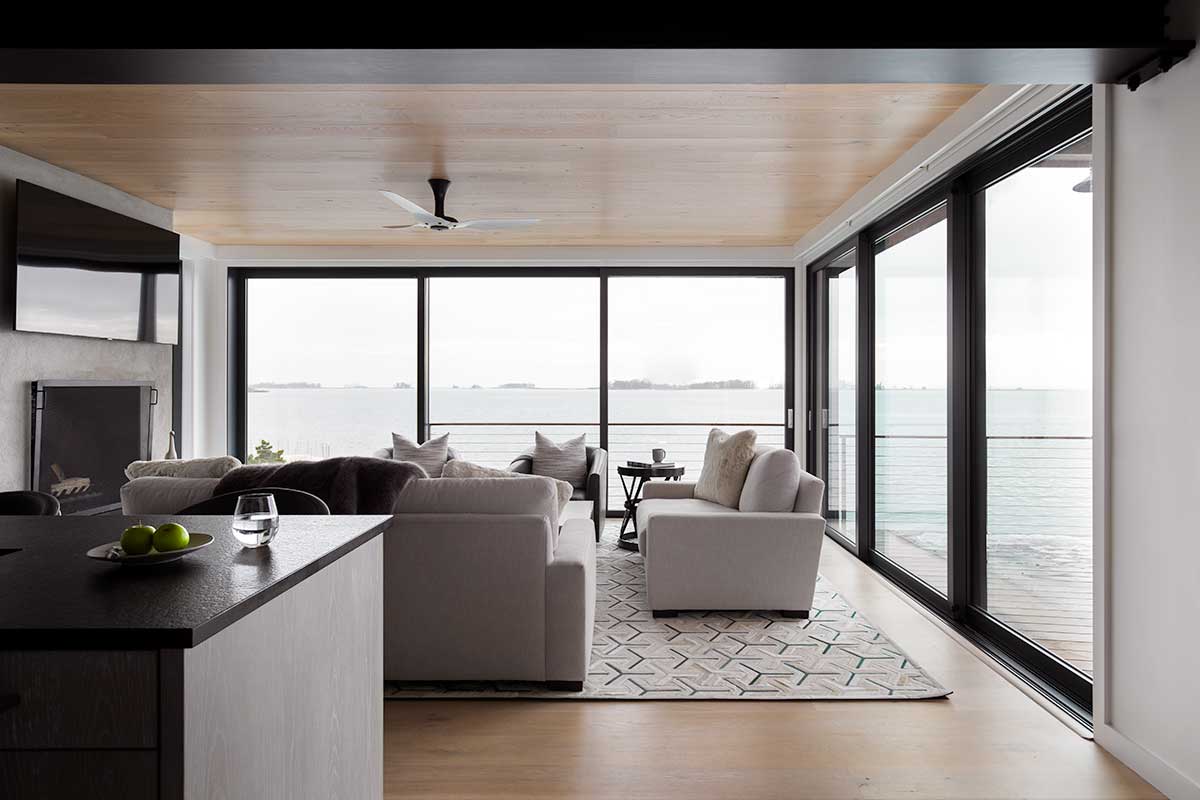 A living room and kitchen of a modern home, featuring a Marvin Modern Multi-Slide door overlooking a body of water.
