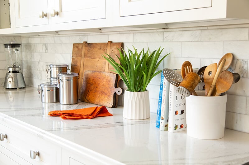 A kitchen counter with a plant, small appliances, cutting boards, and cookbooks.