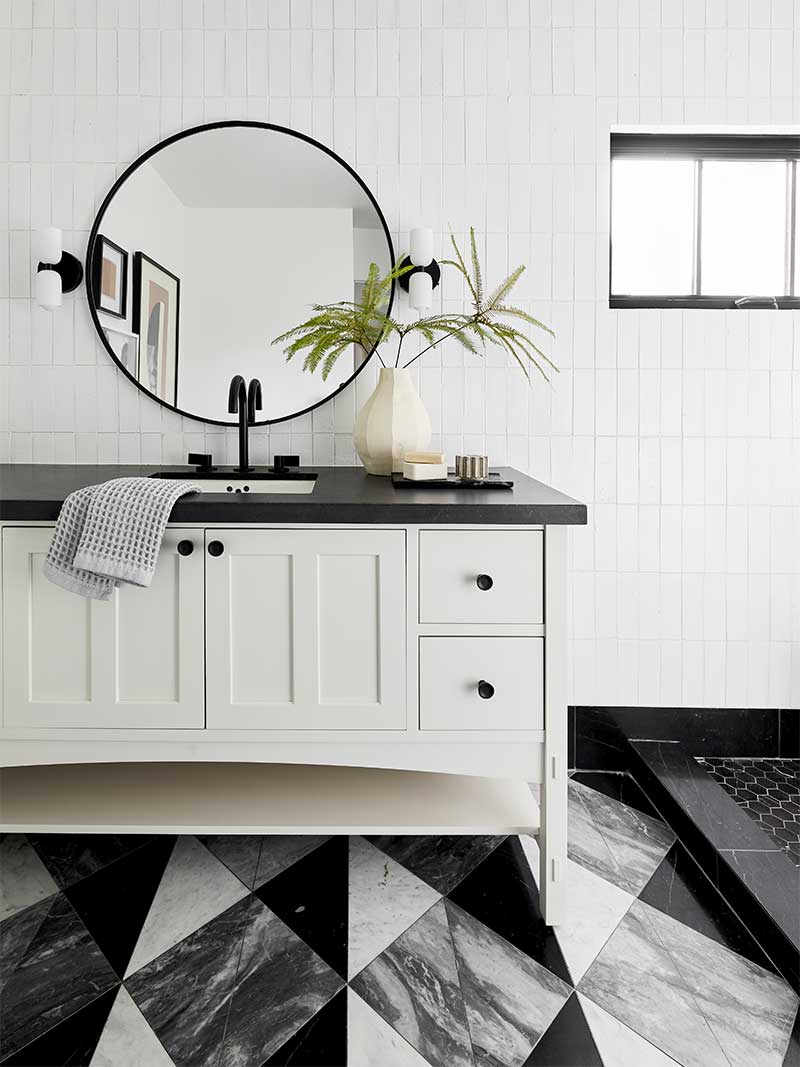 A modern bathroom with black countertop, white cabinets, a Marvin Ultimate Awning window and geometric floor tiles.