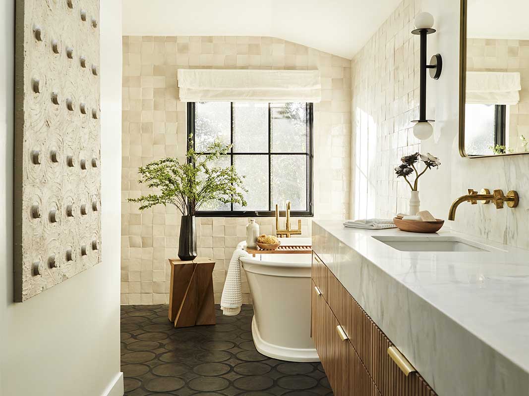 A large bathroom with Spanish influences, multiple types of tile, gray and white marble countertop with bamboo cabinets, bathtub and a Marvin Ultimate Casement window.