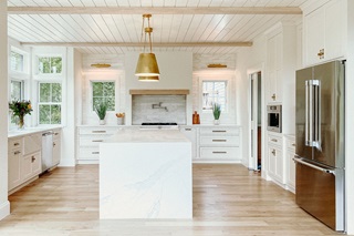 A modern white kitchen featuring live edge waterfall island and Marvin Elevate casement and double hung windows.