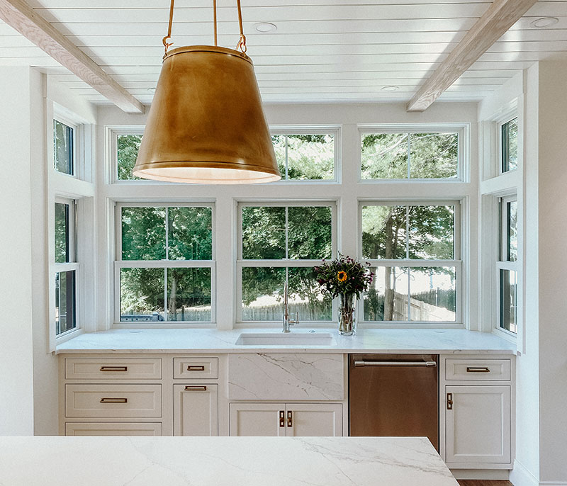 A modern white kitchen featuring Marvin double hung and casement windows and live edge waterfall island.
