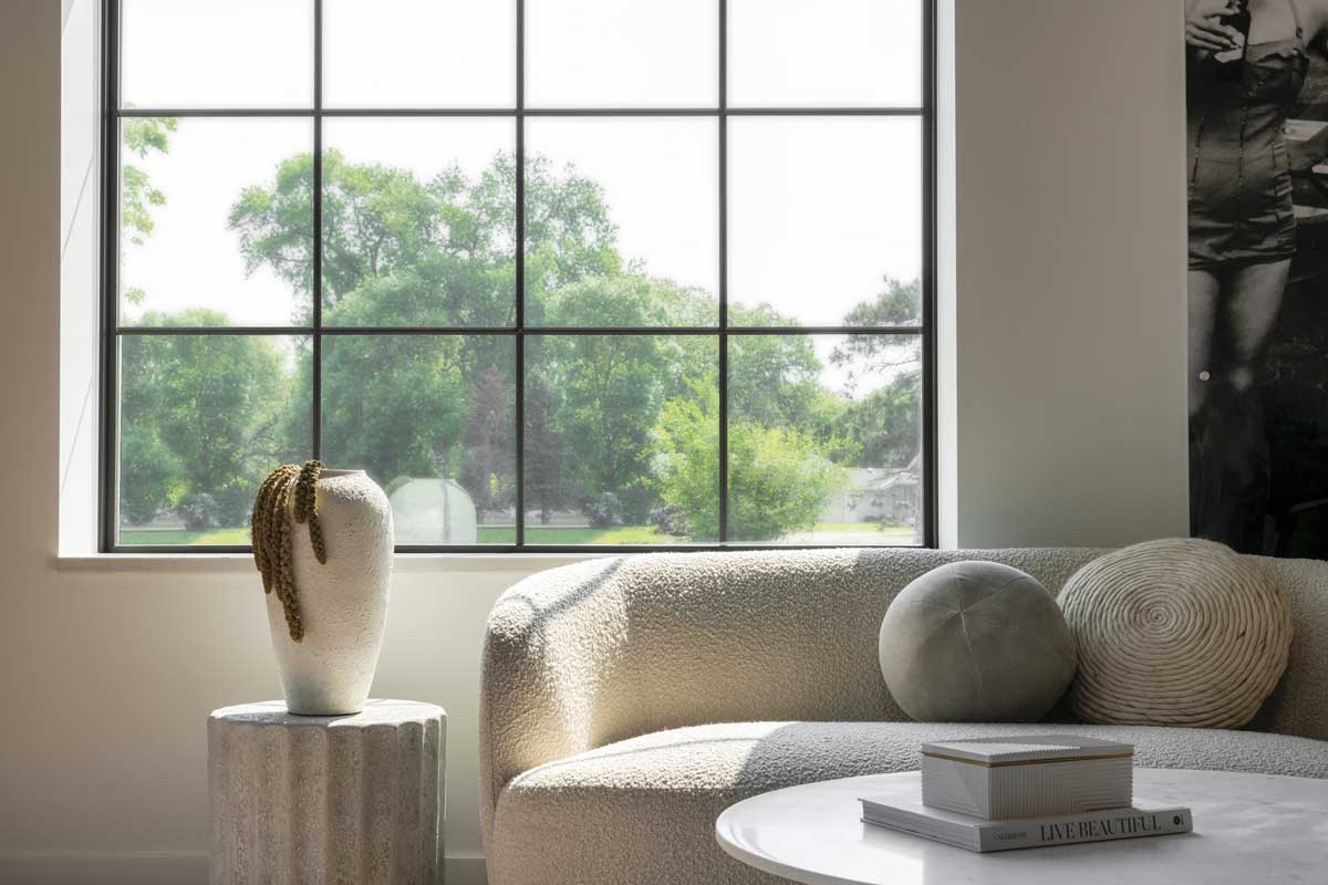 A sitting room at the Adorned Homes office with a large Marvin Essential Direct Glaze window, a white couch, side table with vase and round coffee table.