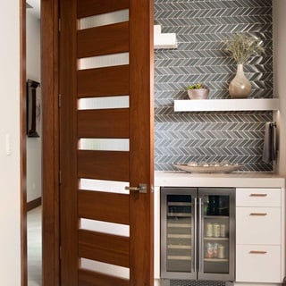 An open TruStile door that leads into a breakfast nook with wet bar with zigzag tile and open shelving on the wall.