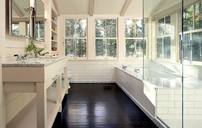 A white bathroom featuring glass shower door, white tile and Marvin double-hung windows.