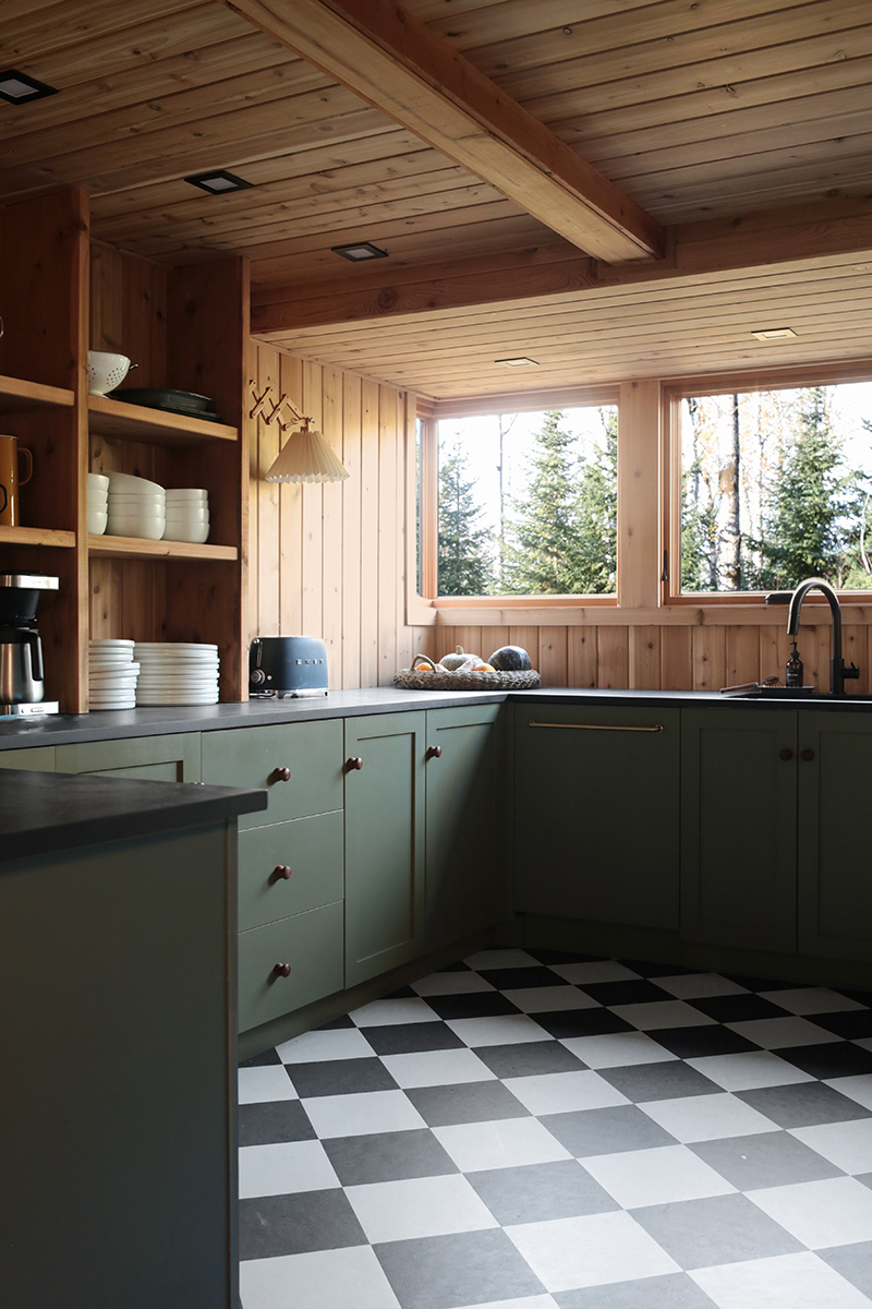 The kitchen of The Minne Stuga, with Marvin Ultimate windows, sage green cabinets and black and white checkered flooring.
