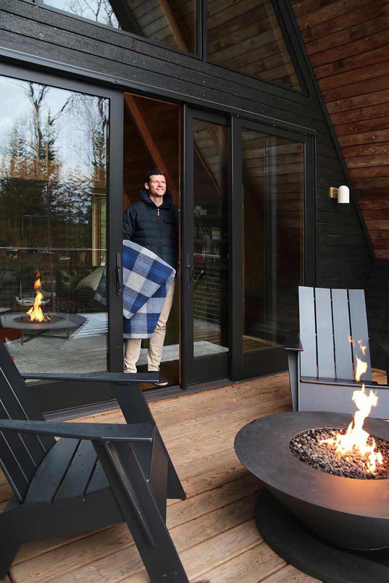 A man holding a blanket, walking out of an A-frame cabin onto the deck through a Marvin Ultimate Sliding French door.