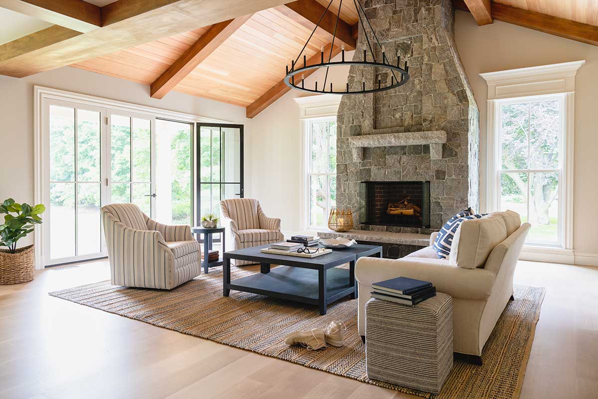 A living room with vaulted ceilings, Marvin windows and doors, and a large stone fireplace inside the Hadley House in Wenham, Massachusetts.