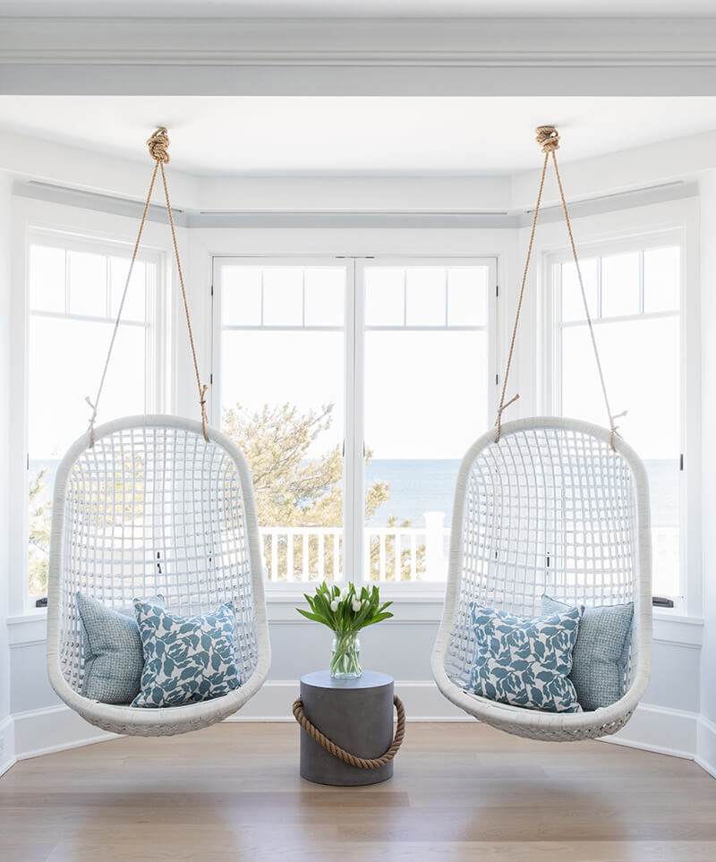 Hanging basket chairs in front of a view of the ocean through Marvin windows.