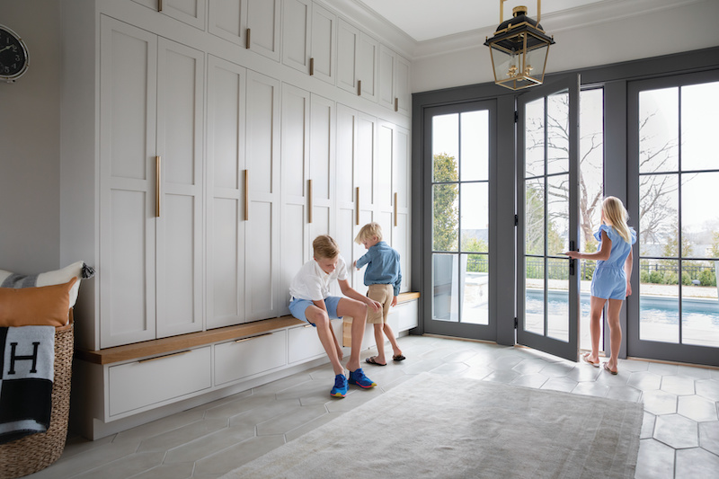 Three children getting their shoes on in a grand mudroom with built in cabinets and Marvin Elevate Inswing French doors.