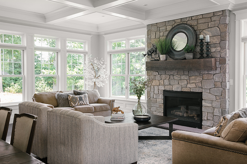 The family room of a contemporary cottage home in New England, featuring Marvin Elevate double hung windows and a stonework fireplace.