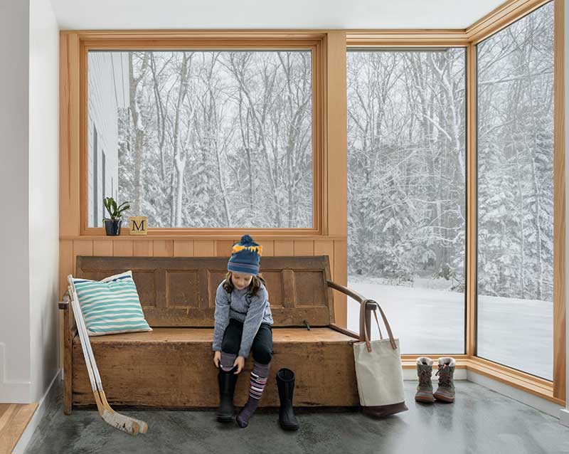 A little girl sits on a bench below a Marvin Elevate Picture window with snow outside.
