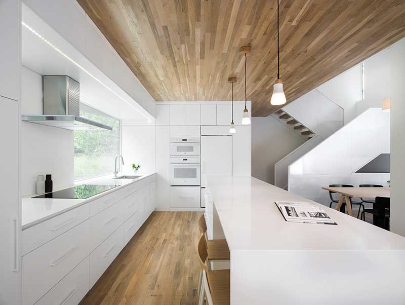 A Nordic-style kitchen with white countertops, wood floors, and a Marvin Essential Picture window. 