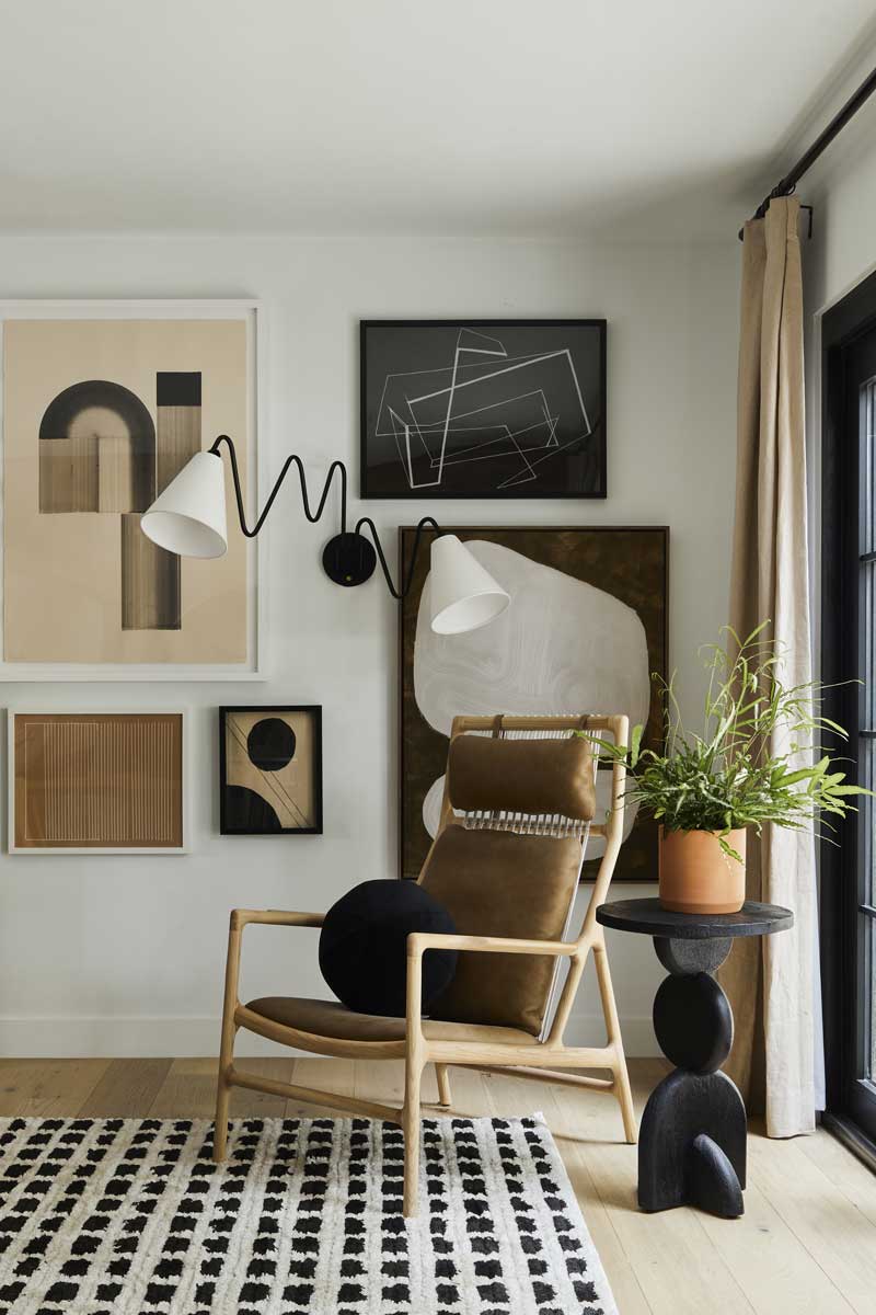 A sitting area in the Bobby Berk Firm’s office space, with a modern chair, art, lamp and side table next to a Marvin Ultimate Outswing French door G2.