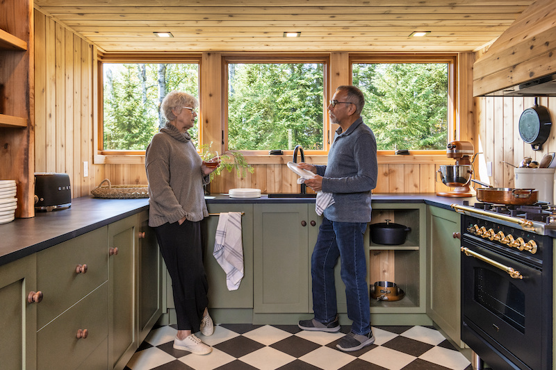 An older couple standing in the kitchen of The Minne Stuga, in front of three Marvin Ultimate Awning windows.