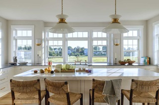 A bright kitchen with white marble countertops and vegetables being prepped in front of Marvin Elevate Double-Hung windows overlooking a marsh.