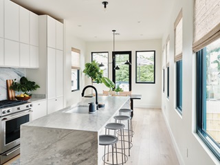 Kitchen with stone island and bar stools in contemporary home, featuring Marvin Essential Casement window and Marvin Essential Casement Picture window
