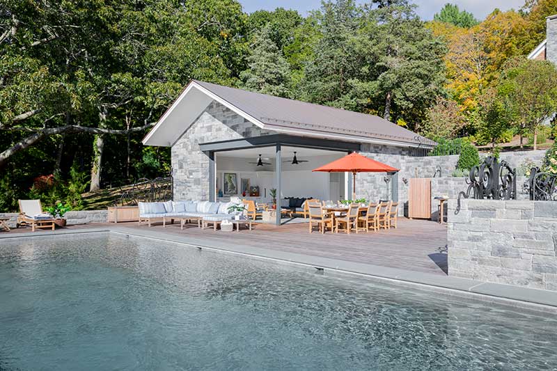 A swimming pool and stone pool house featuring the Marvin Ultimate Multi-Slide Corner door. 