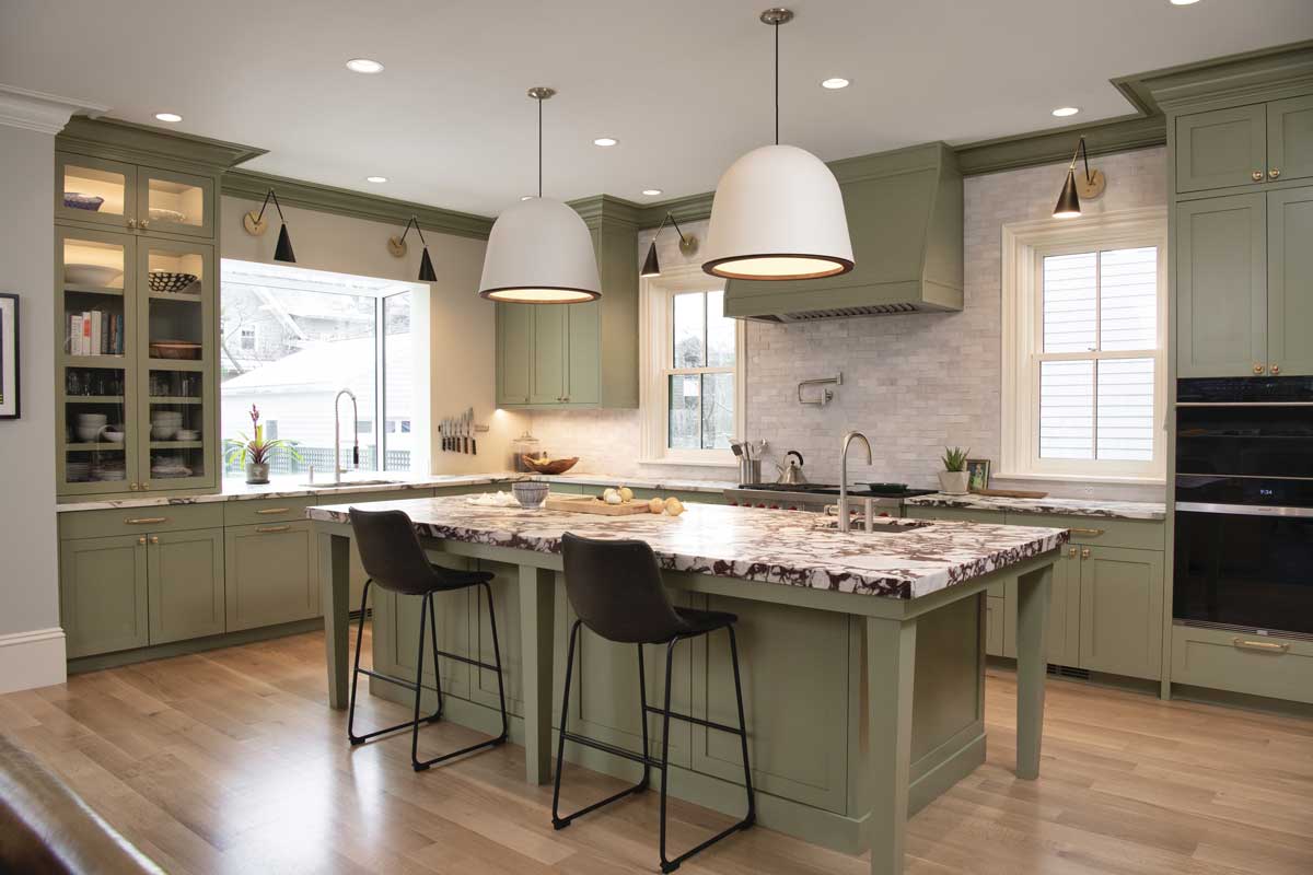 A contemporary kitchen with black and white marble countertops, sage green cabinets and a Marvin Skycove above the sink.
