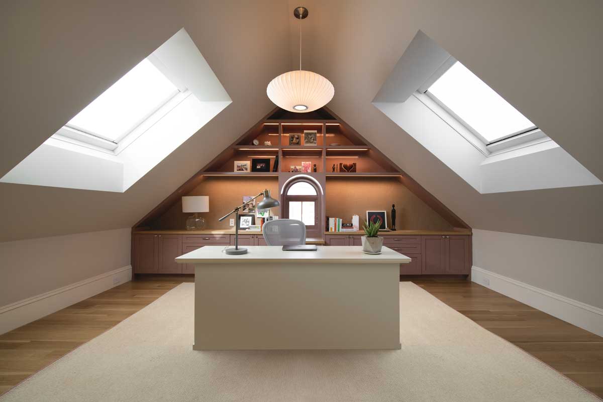 An office space with two Marvin Awaken Skylights, a hanging lanter, rose-colored built-ins and a modern desk in the center of the room.
