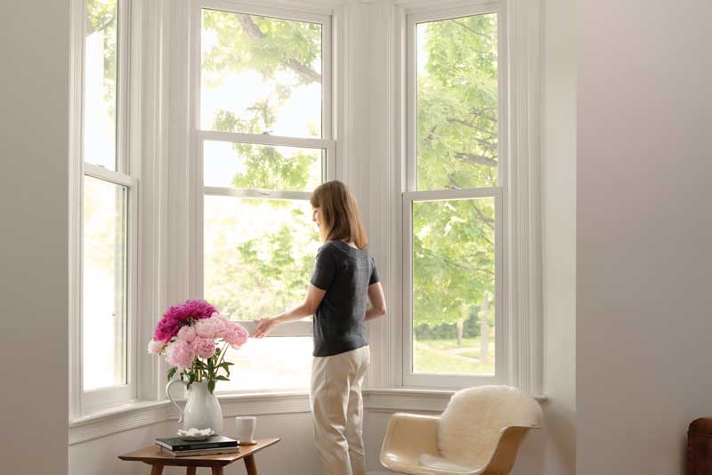 Woman opening a white Marvin Ultimate Double Hung window in a home