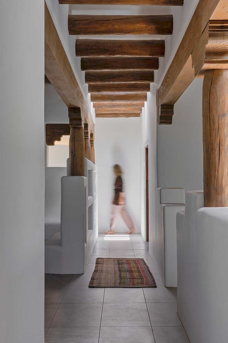Jules Moore walking across a hallway in her Pueblo-style home in Santa Fe, New Mexico with bullnose edges and wood beams.