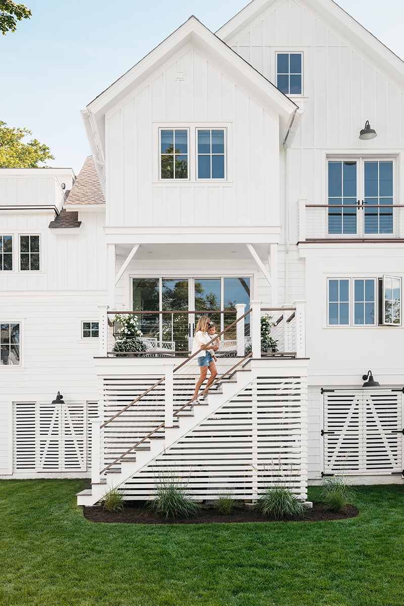 The back of Liz Joy’s remodeled home in Connecticut, featuring Marvin Elevate windows and doors, where she’s carrying her child up a staircase.