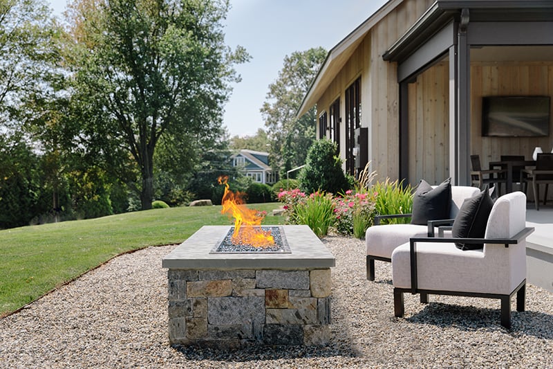 An outdoor fireplace near the porch of a modern farmhouse in Norwalk, Connecticut, featuring Marvin windows and doors.