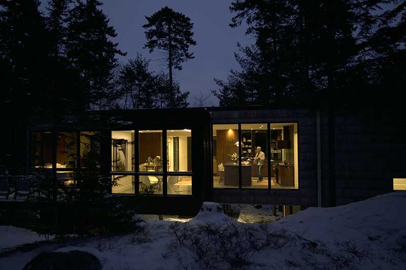 An exterior photo at night looking into the kitchen of a modern cabin in Maine featuring Marvin Ultimate windows and doors.