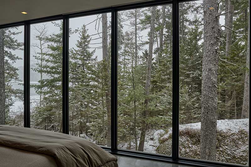 A wall of floor-to-ceiling Marvin Ultimate Picture windows in a bedroom looking out on a snowy forest landscape.