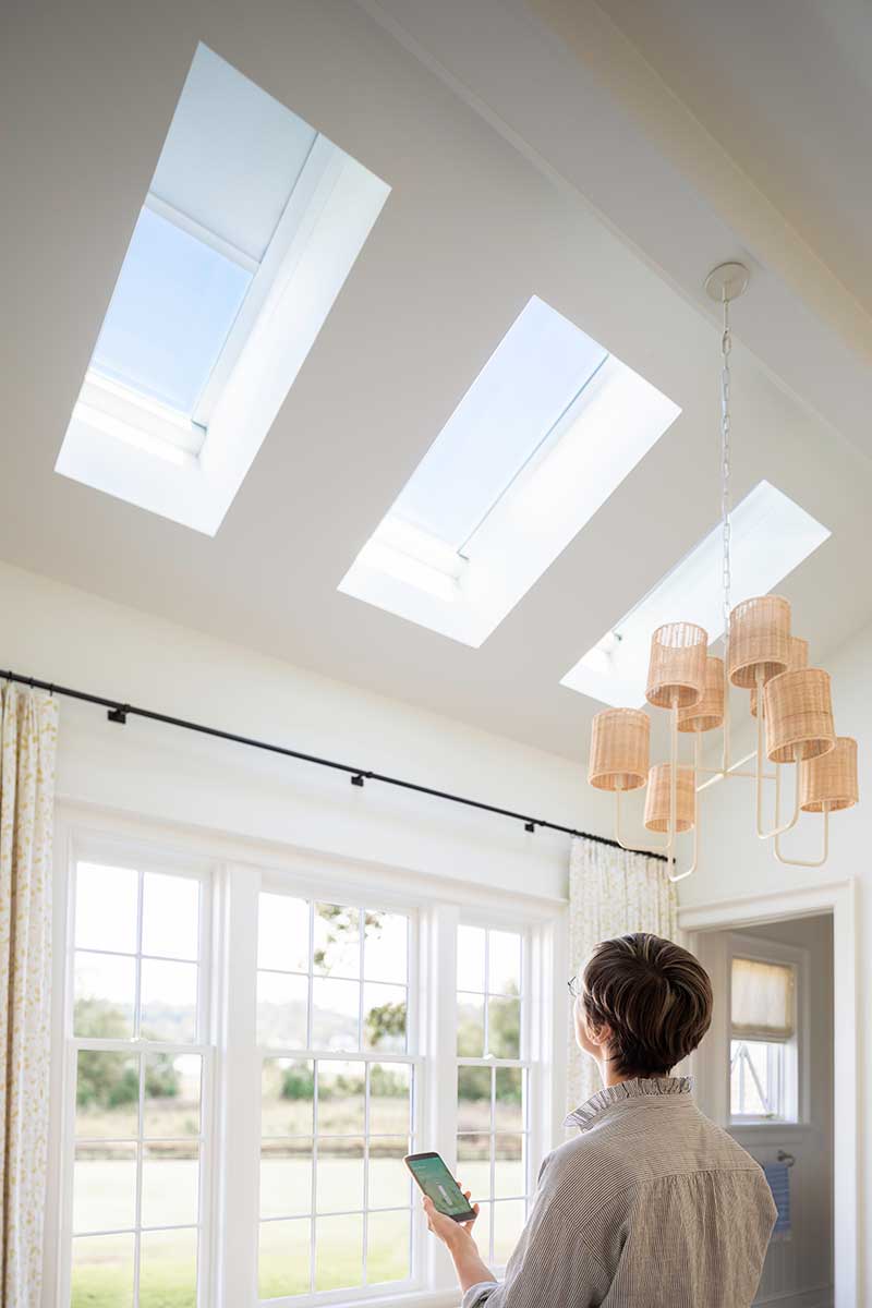 A woman closing the shades on three Marvin Awaken Skylights in a bedroom in the Southern Living Idea House in Kentucky.