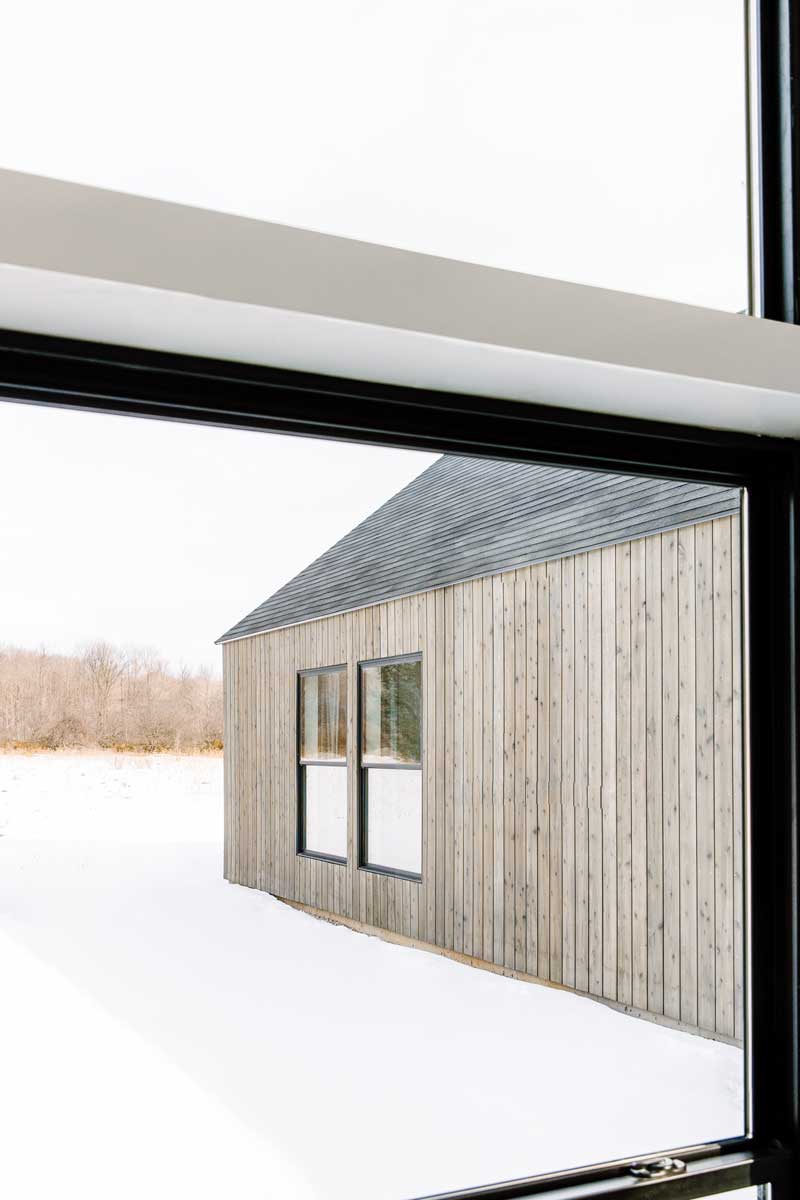 A close up view looking out the window of the main building of Svart Hus and showing the vertical slats of the natural wood clad adjacent unit against the snowy landscape. 