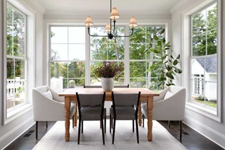 A dining room surrounded by Marvin Essential double hung windows on three sides with a hanging light, table, and chairs.