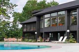 A resort-style pool with pink and white mid-century pool furniture against the backdrop of a black home in Minnesota with Marvin Essential windows.