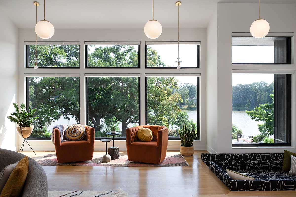 A modern sitting area with two dark orange chairs that overlooks a tree-lined lake thorugh Marvin Essential windows.