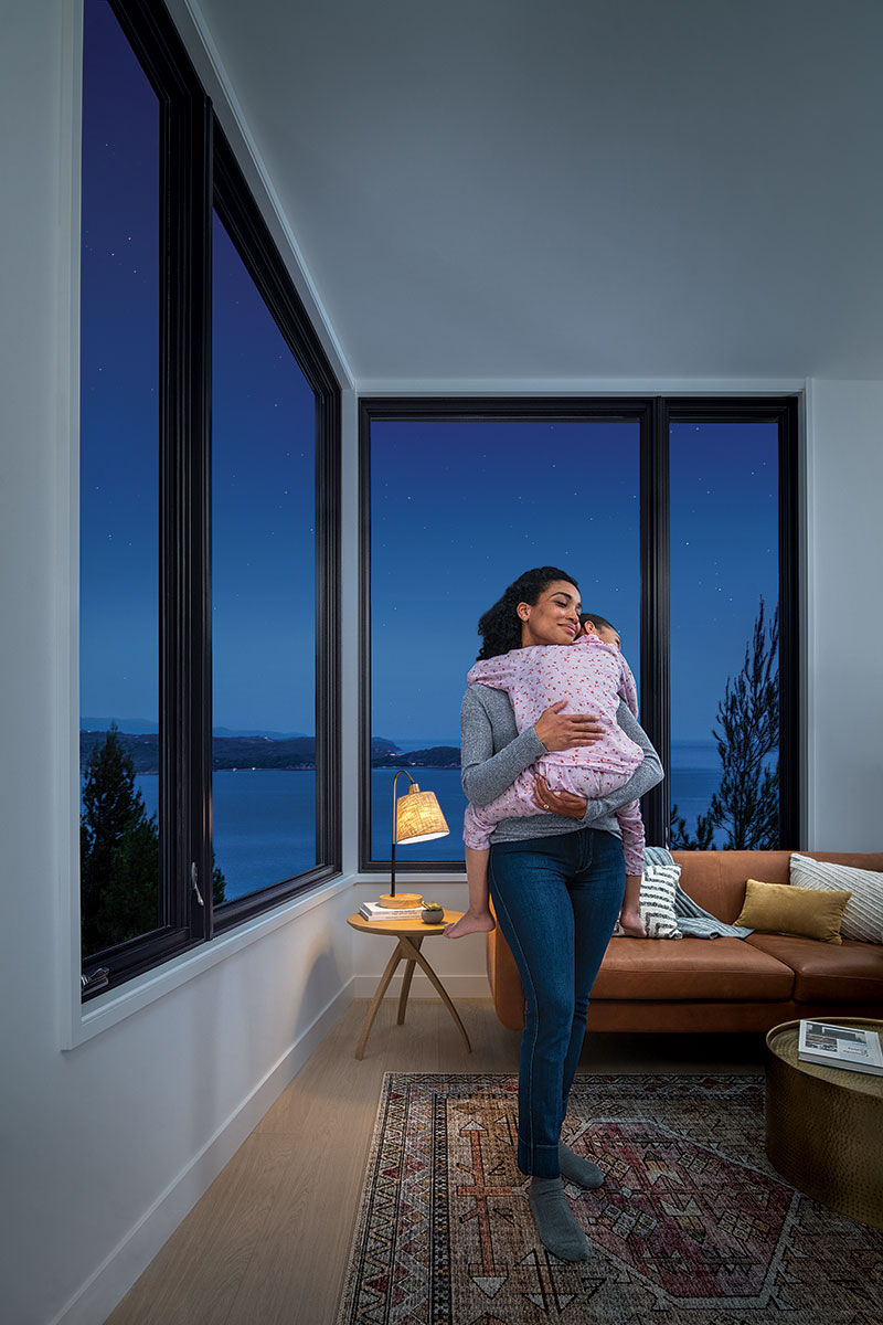 A woman holding a sleeping girl with a view of a dark night through the Marvin windows behind them.