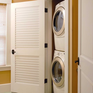 A TruStile louvered door opened to reveal a stacked washer and dryer.