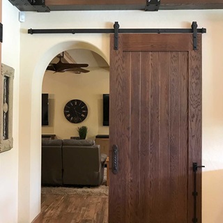 A dark brown plank panel TruStile barn door leading into a living room.