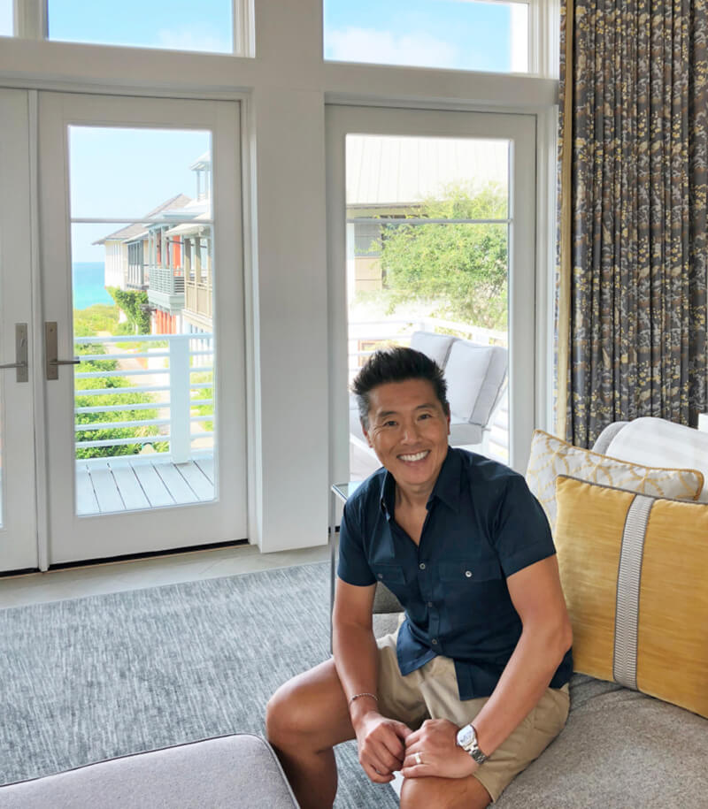 Vern Yip sitting on couch in front of large Marvin Windows at his beach home