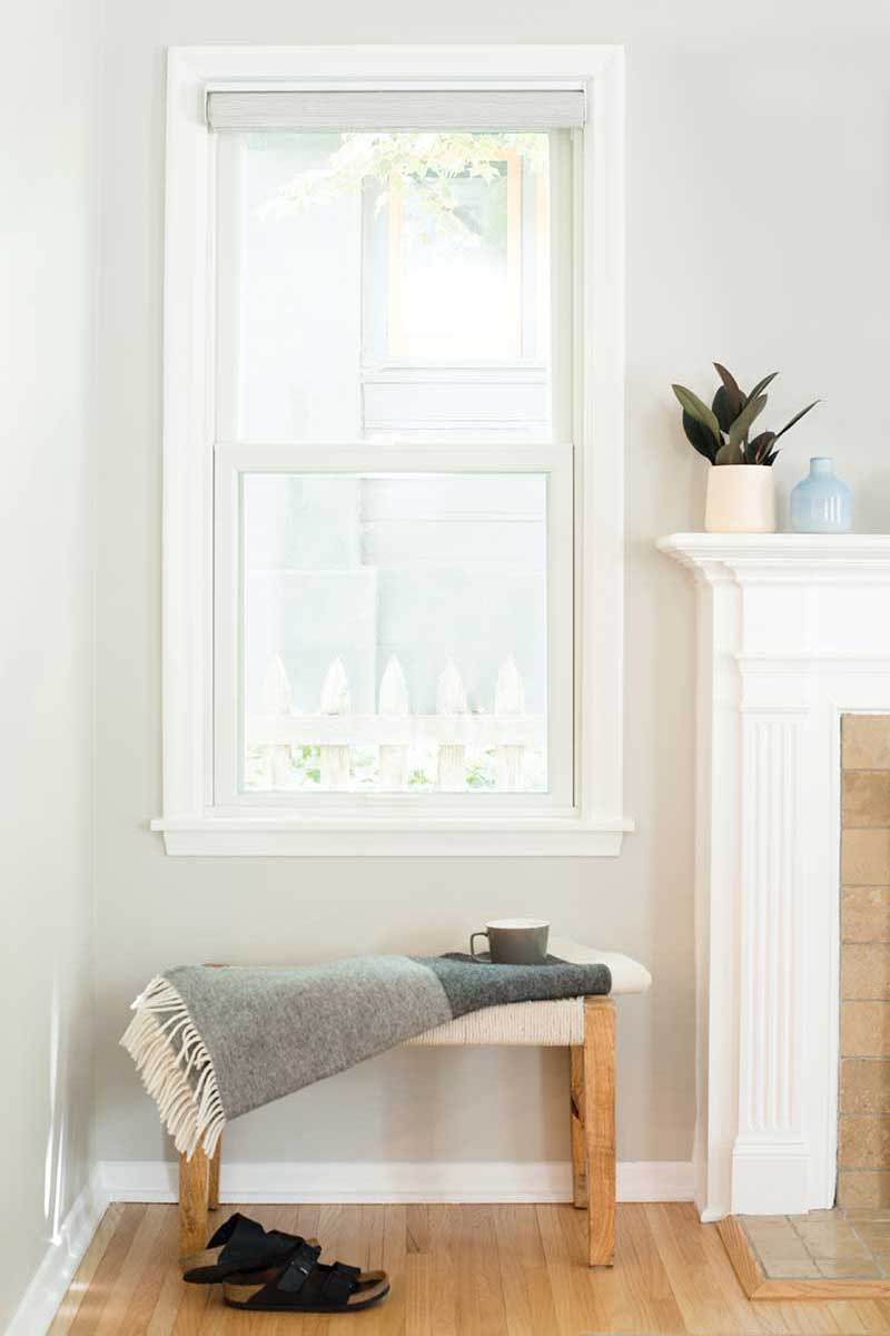 A bench next to a white fireplace below a white Marvin double hung window.