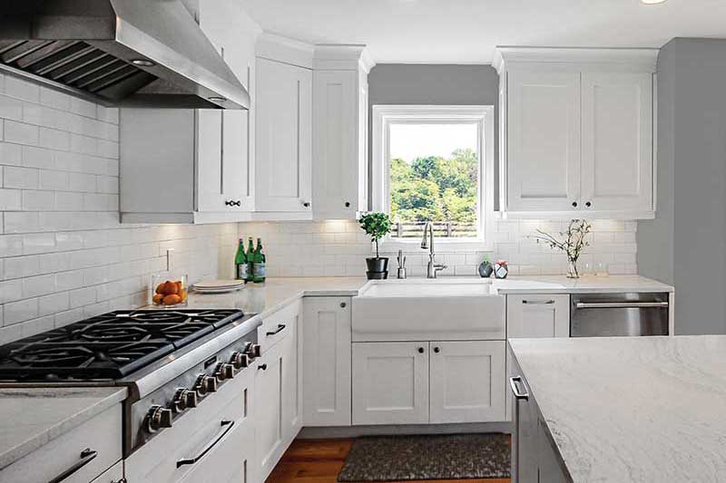 A modern kitchen featuring a large range with hood, light countertops, white cabinets and a Marvin picture window.