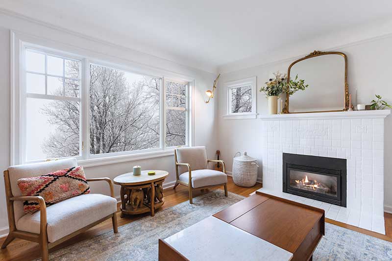 A bright living room in winter with white brick fireplace and Infinity by Marvin picture windows.