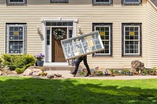 man carrying fiberglass replacement window in front of a house